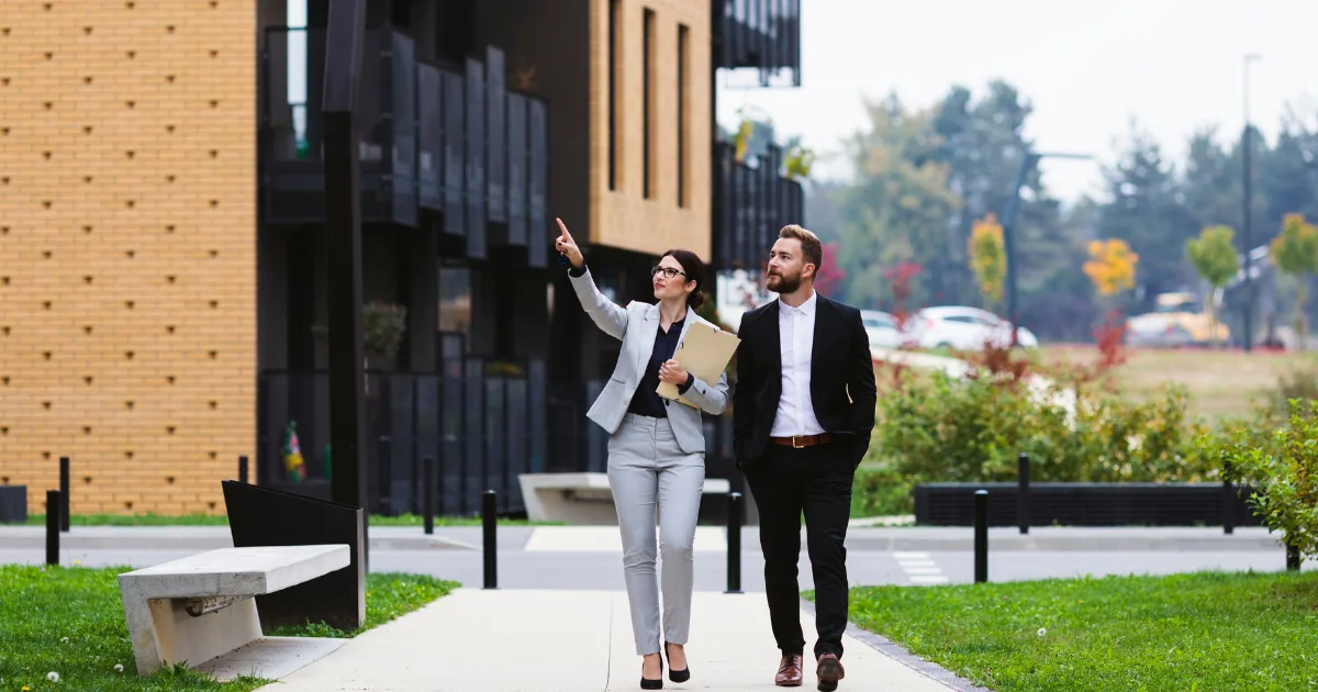 Two professionals walking and talking outside apartment buildings