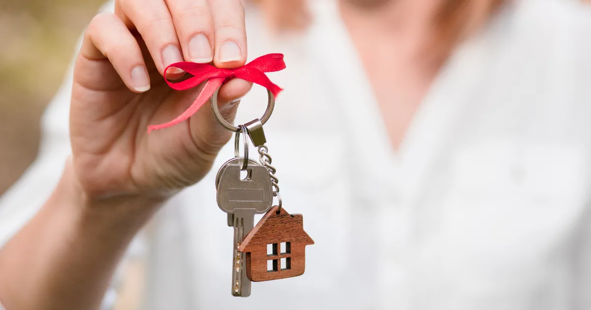 Hand holding house keys tied with a red ribbon