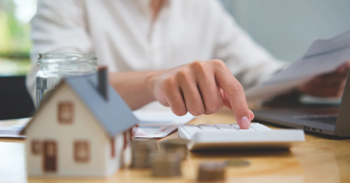 Person using a calculator beside a model house and papers