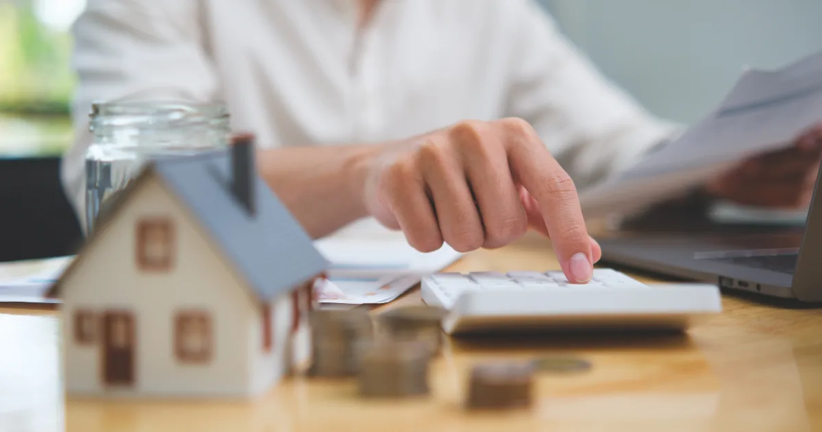 Person using a calculator beside a model house and paperwork