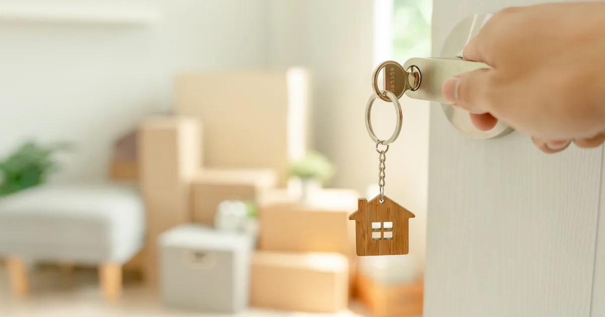 Hand unlocking a door with a house-shaped keyring, with boxes inside the room