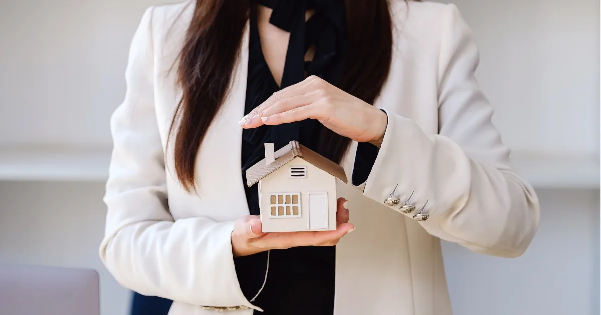 Woman in a white blazer cupping a small model house in her hands