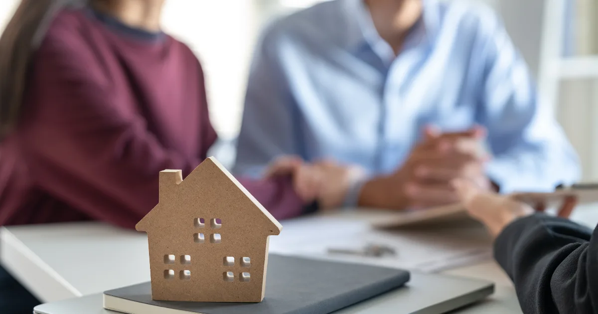 Wooden model house on a desk in front of two people in discussion