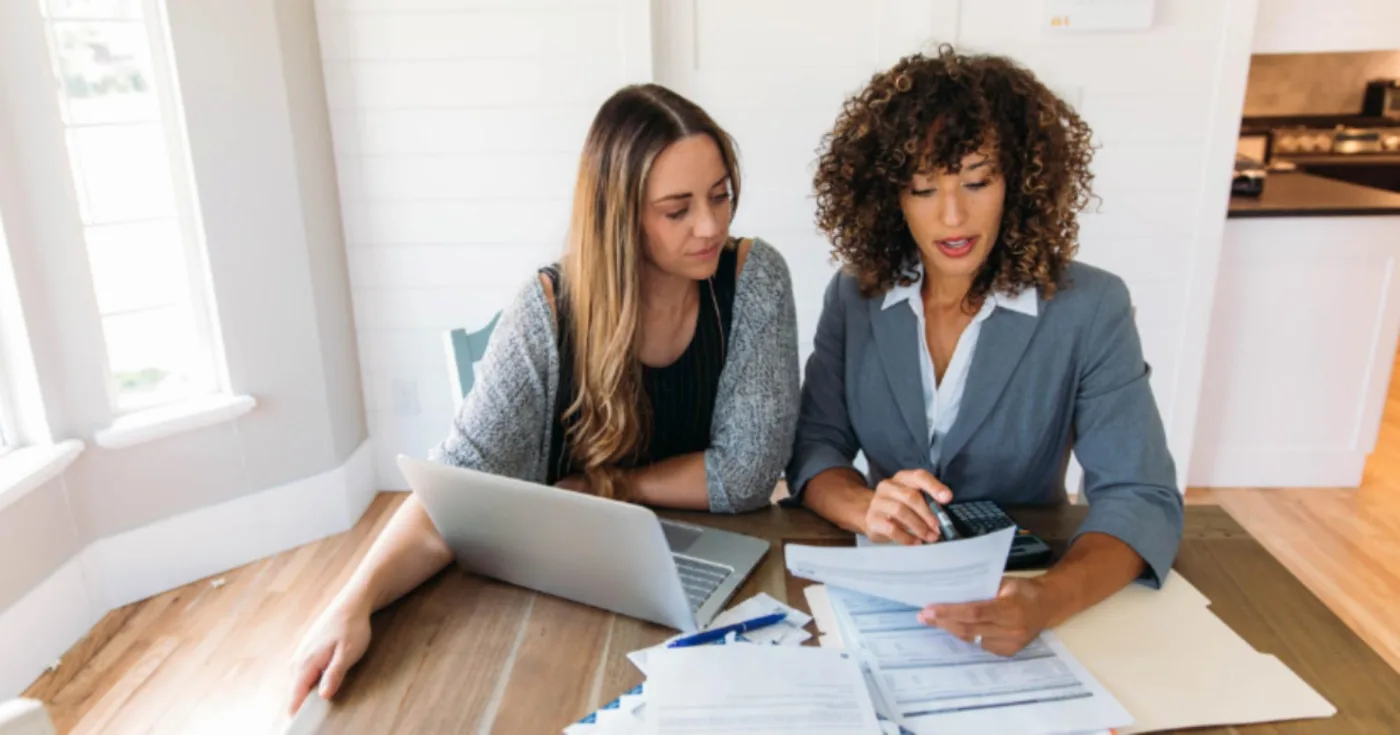 Two women reviewing documents together at a table with a laptop