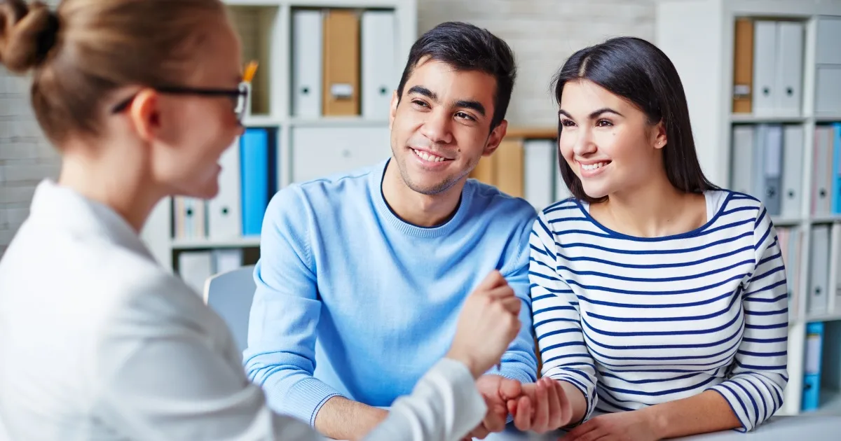 Couple smiling and shaking hands with an adviser in an office