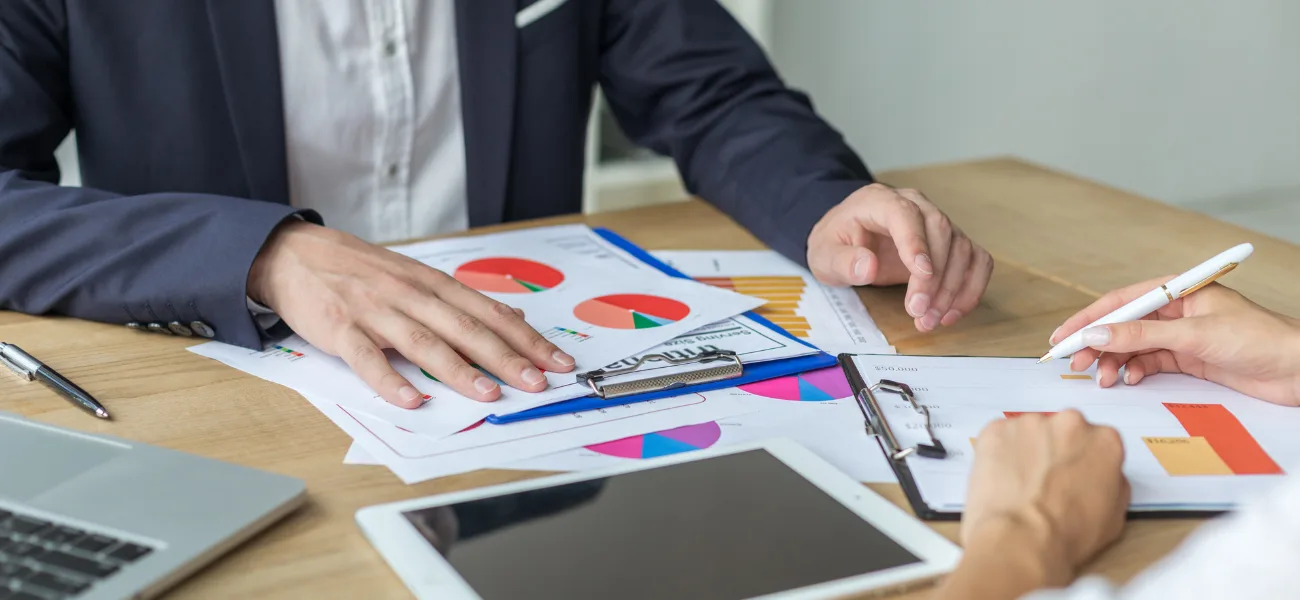 Hands over printed charts and a tablet at a meeting table