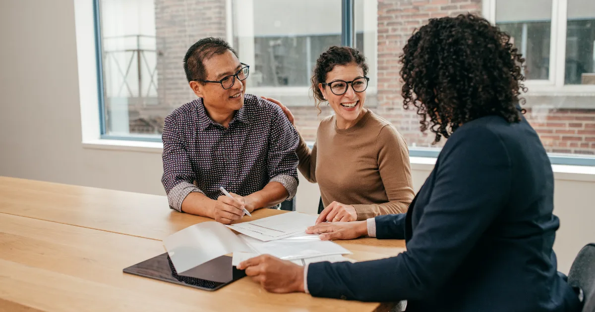 Couple signing documents with an adviser at a table